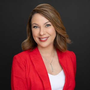 AIC CEO, Amina Deiab pictured in a red blazer and photographed against a grey background