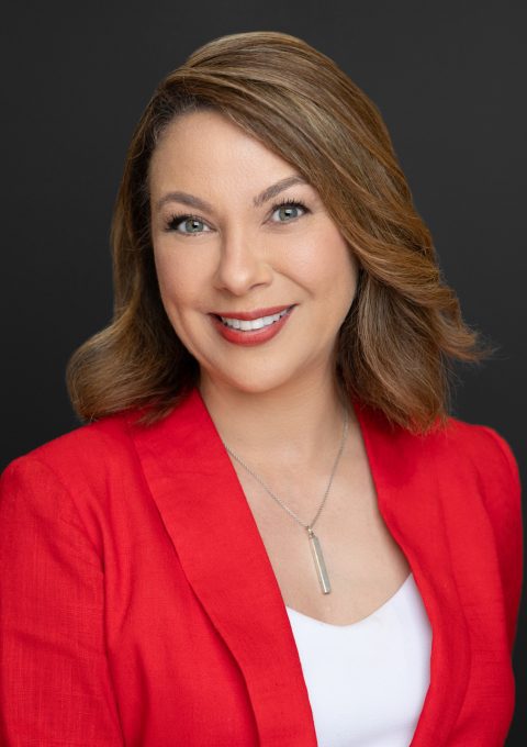 AIC CEO, Amina Deiab pictured in a red blazer and photographed against a grey background