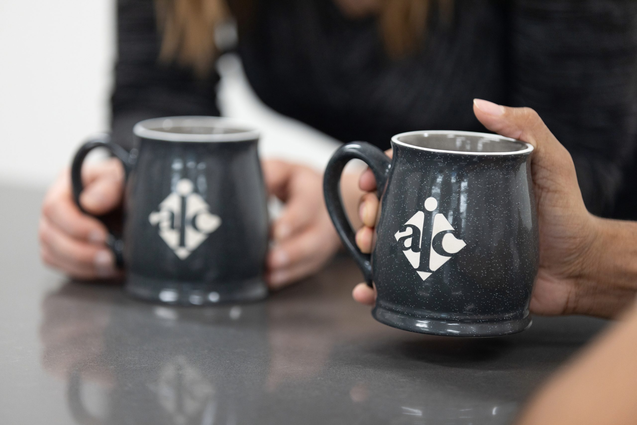 Two AIC employees chatting during a break while holding AIC mugs